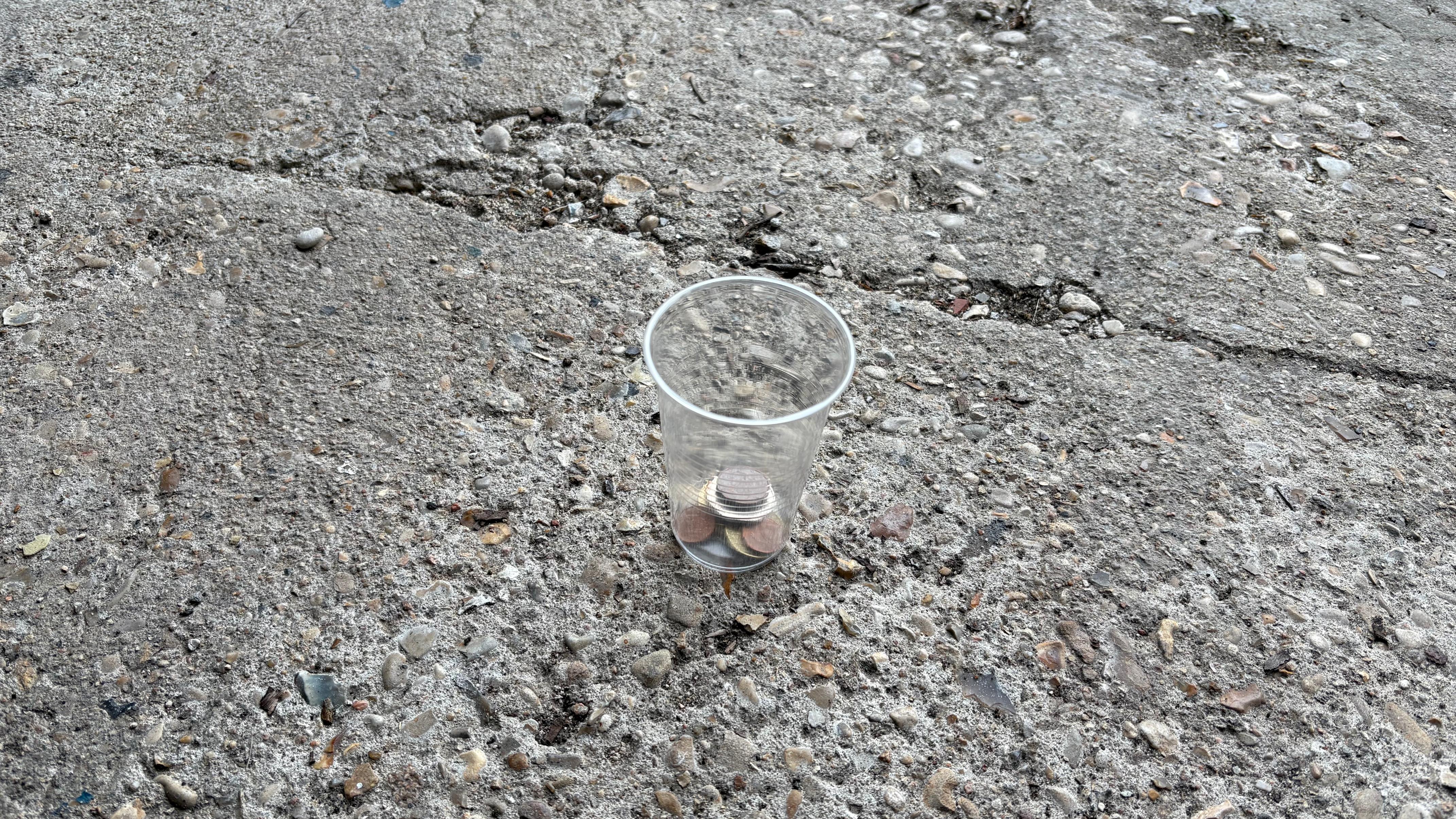 a clear plastic cup on the ground with some coins inside