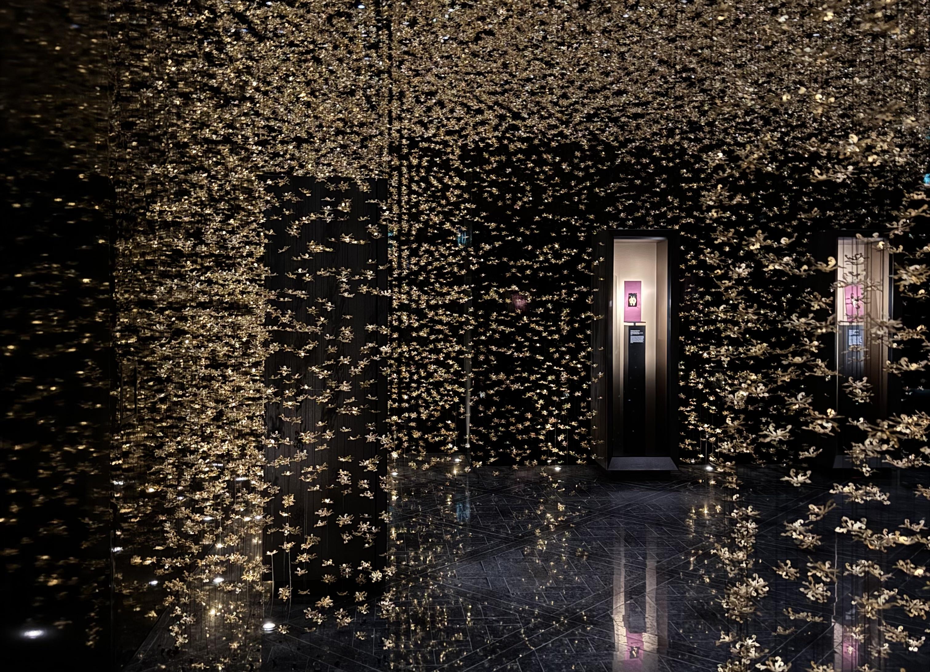 a black room with a hanging display of silver shapes that make the room dance with the lights coming from above. There are two display cases with jewellery in.