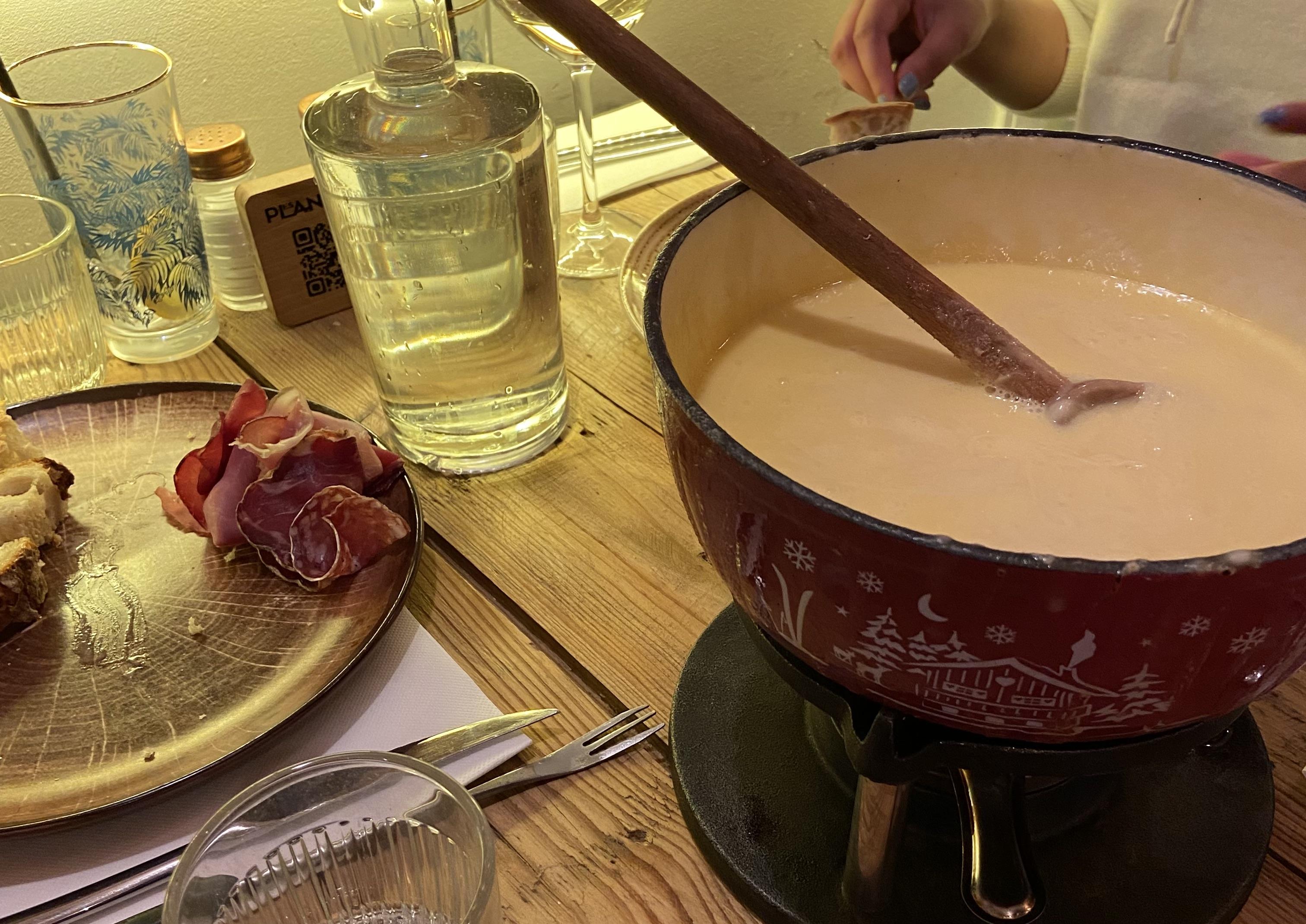 there's a plate on the left that has some bread and meat on. On the right there is a pot of cheese with a wooden spoon in it.