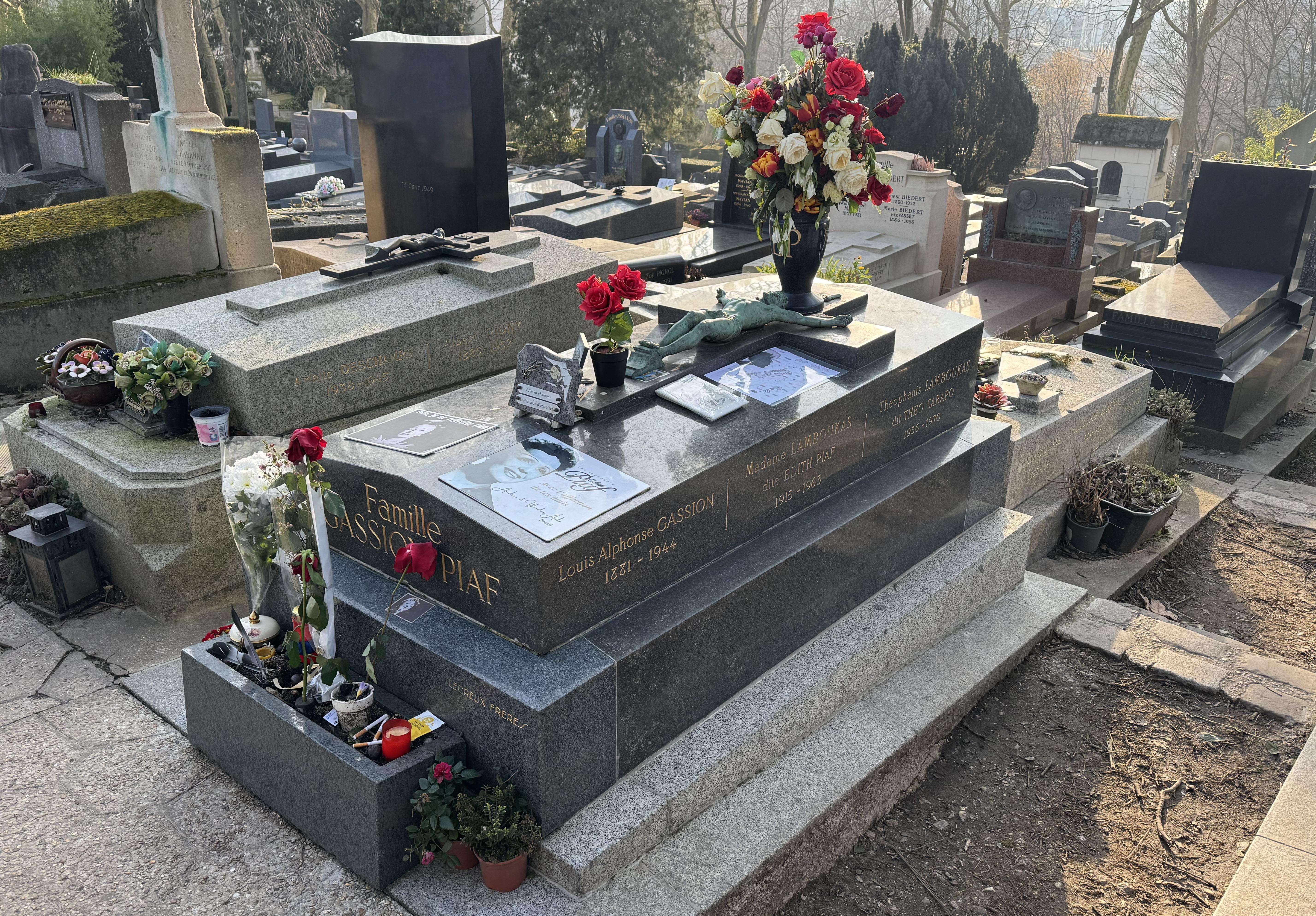 The grave of Edith Piaf. You can see three names along the side, 'Louis Alphonse Gassion, Madame Lamboukas dite Edith Piaf and Théophanis Lamboukas dit Theo Sarapo. There are some items fans have left including red roses