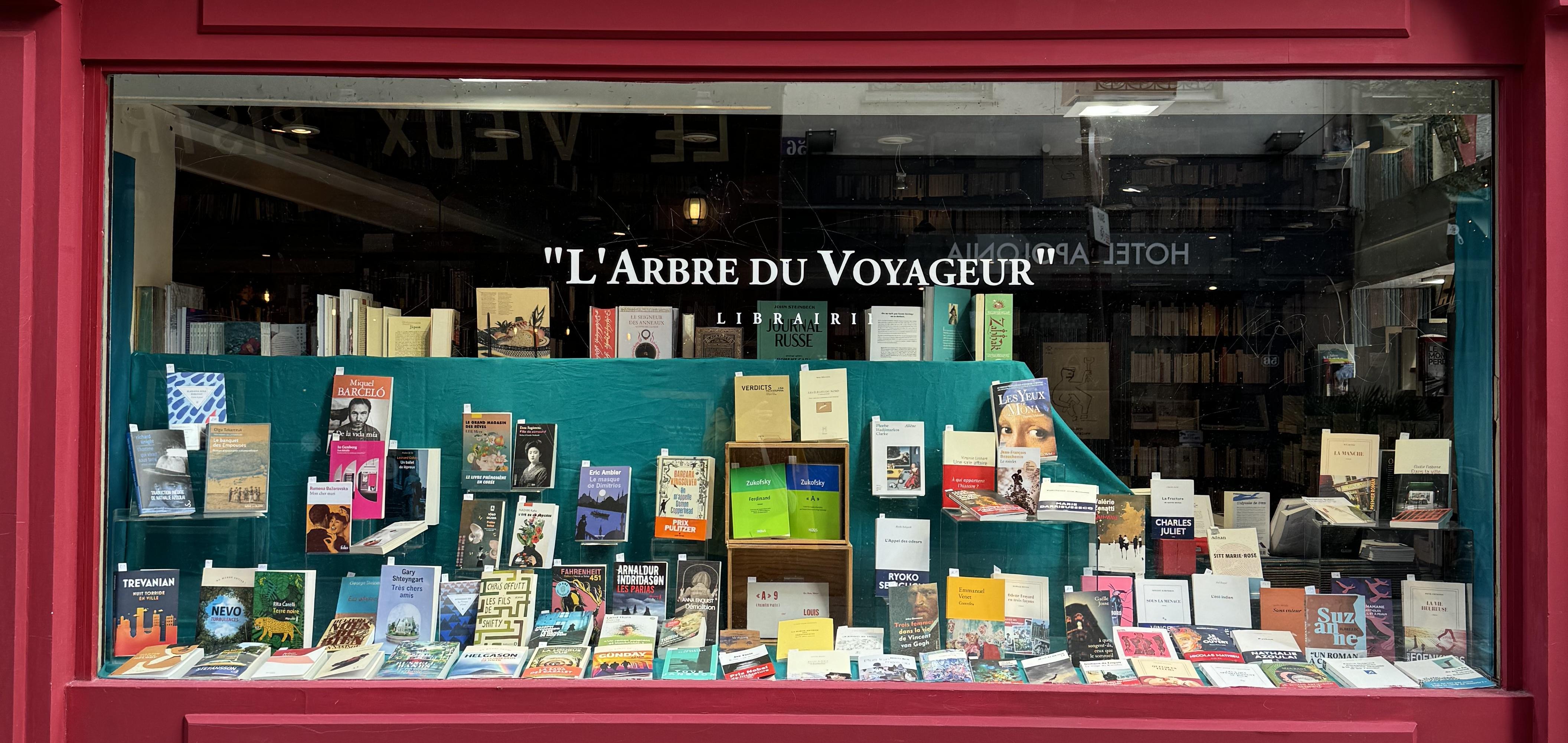 the front of a book store called l'arbre du voyageur. The store has a red front with a big window with books on display