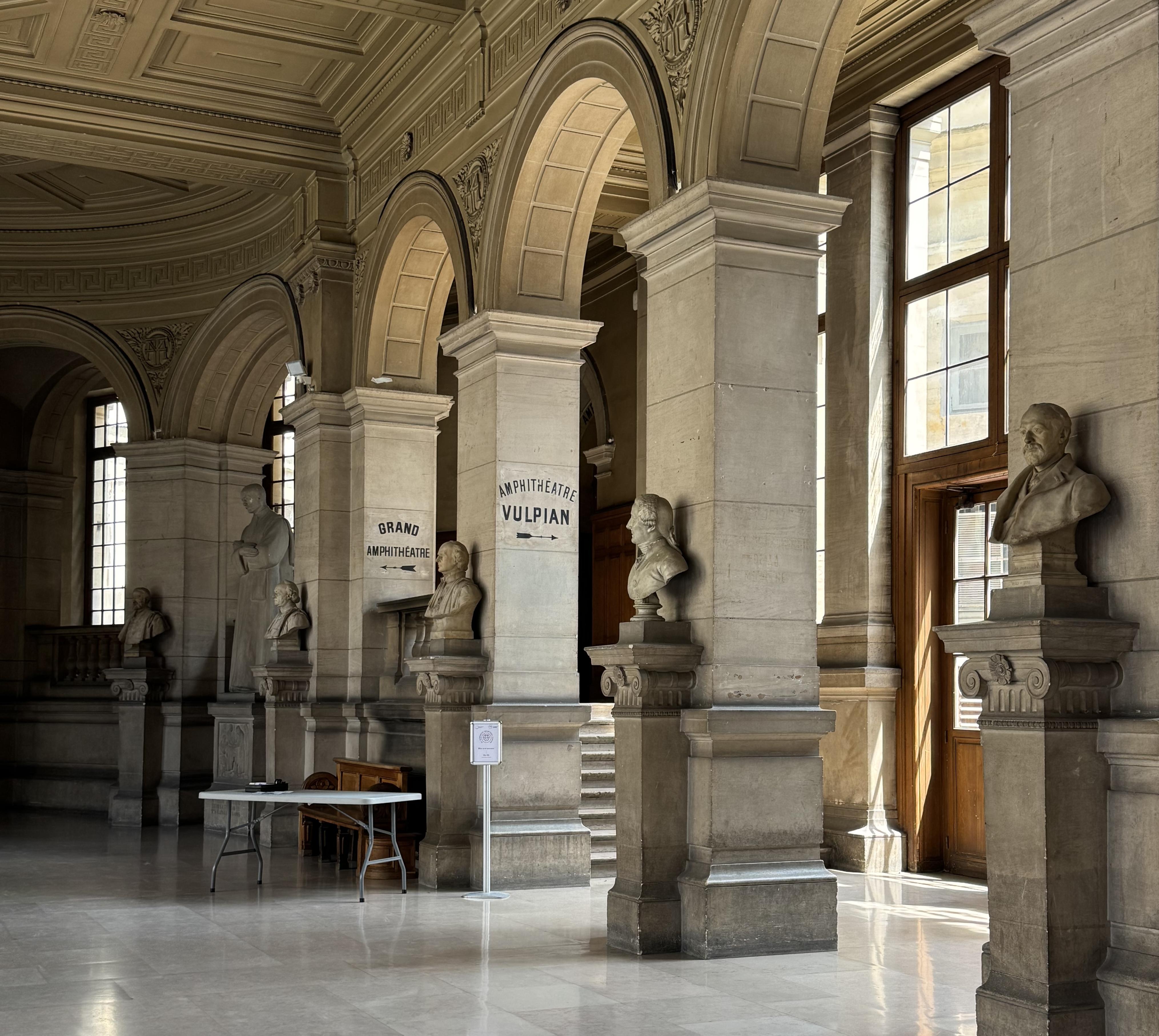 there are five arches. in front of the supporting walls of the arches, there are busts of 5 men. Their names are not readable. On the wall of the arch, there is text that says "AMPHITHEATRE VULPAIN" with an arrow pointing right. on the wall behind, there is text that says "GRAND AMPHITHEATRE" with an arrow pointing left