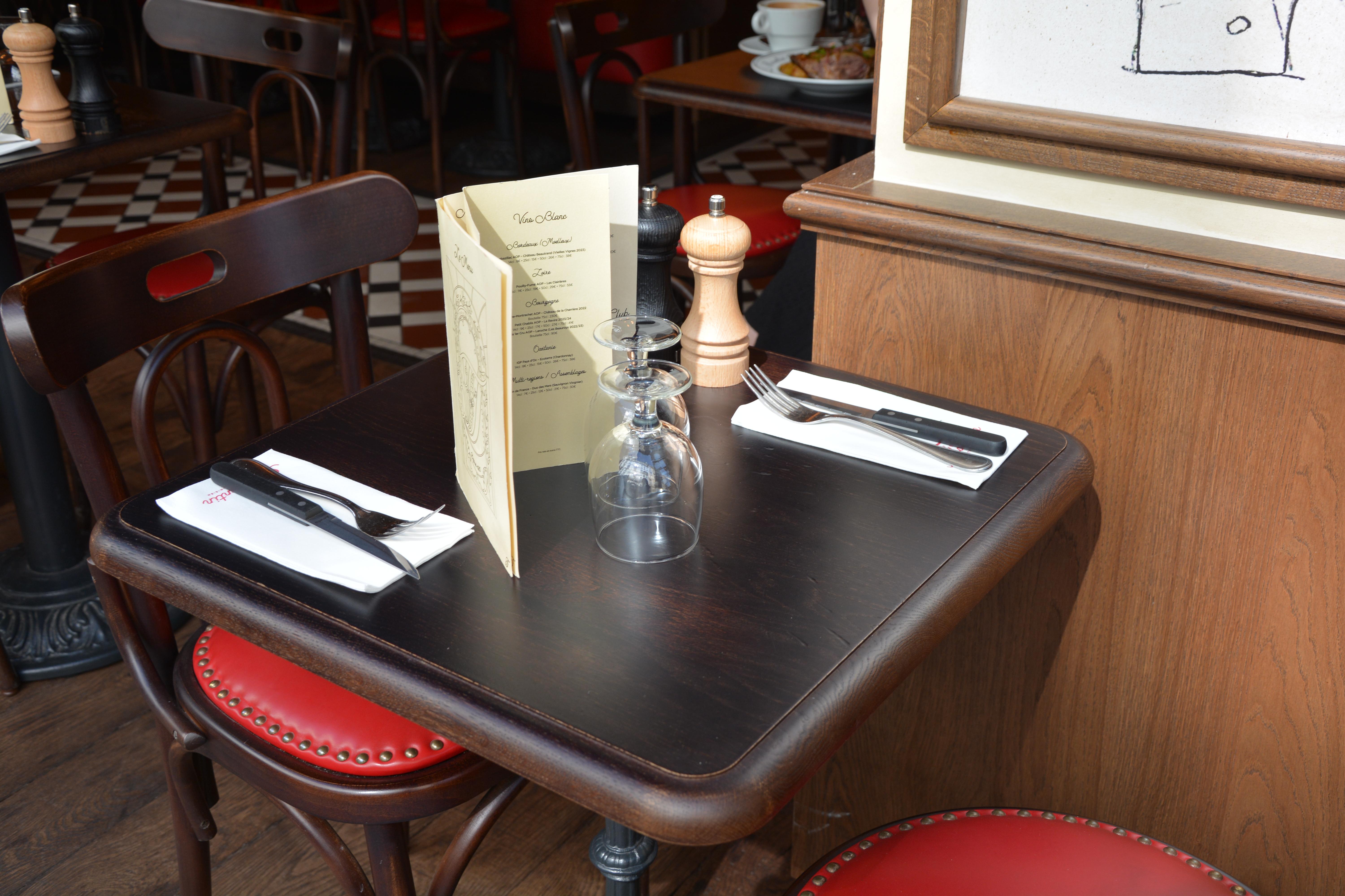 a table for two at a restaurant. On the table there are two wine glasses and two sets of cutlery. There is a menu in the middle of the table.