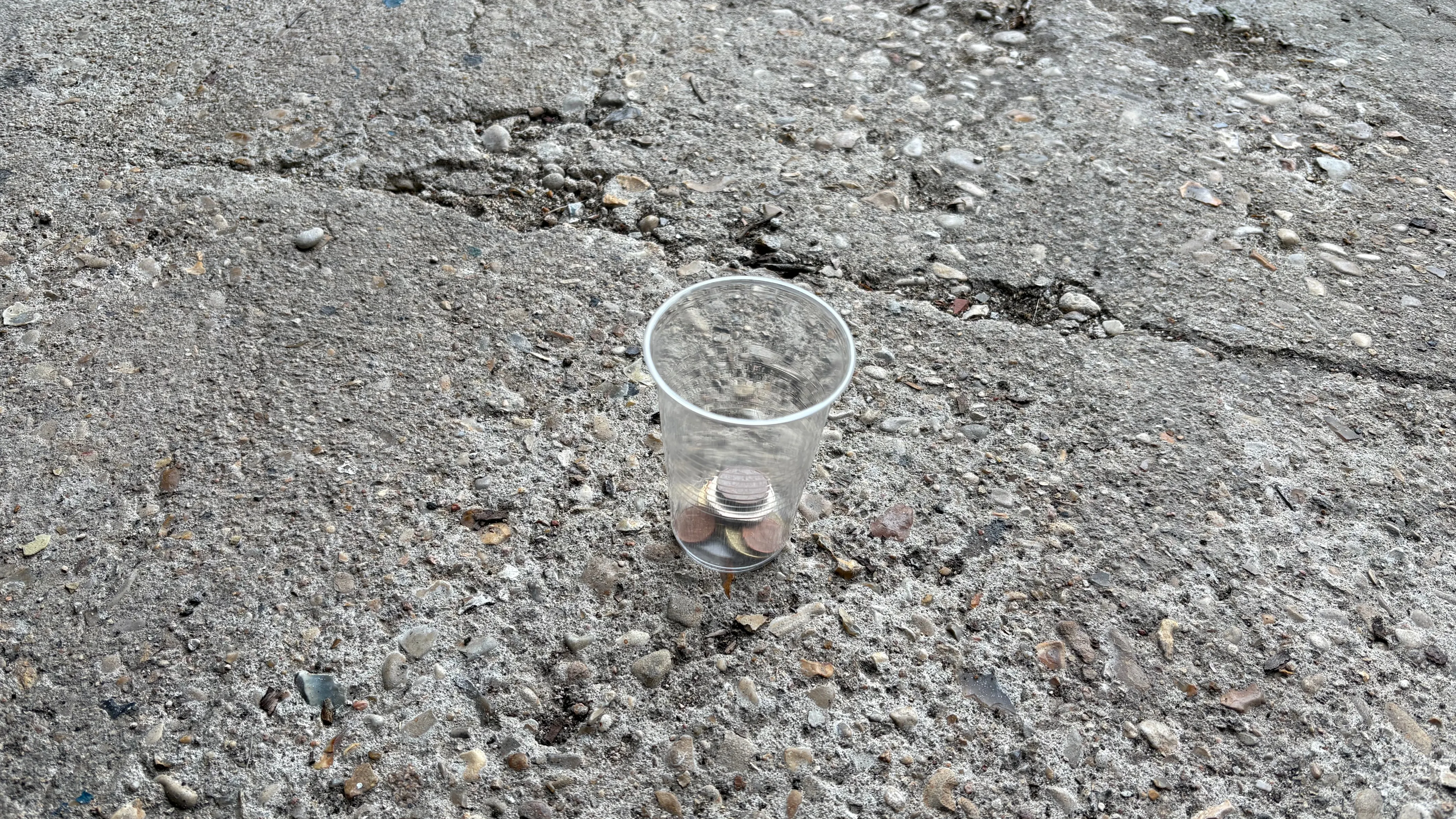 a clear plastic cup on the ground with some coins inside