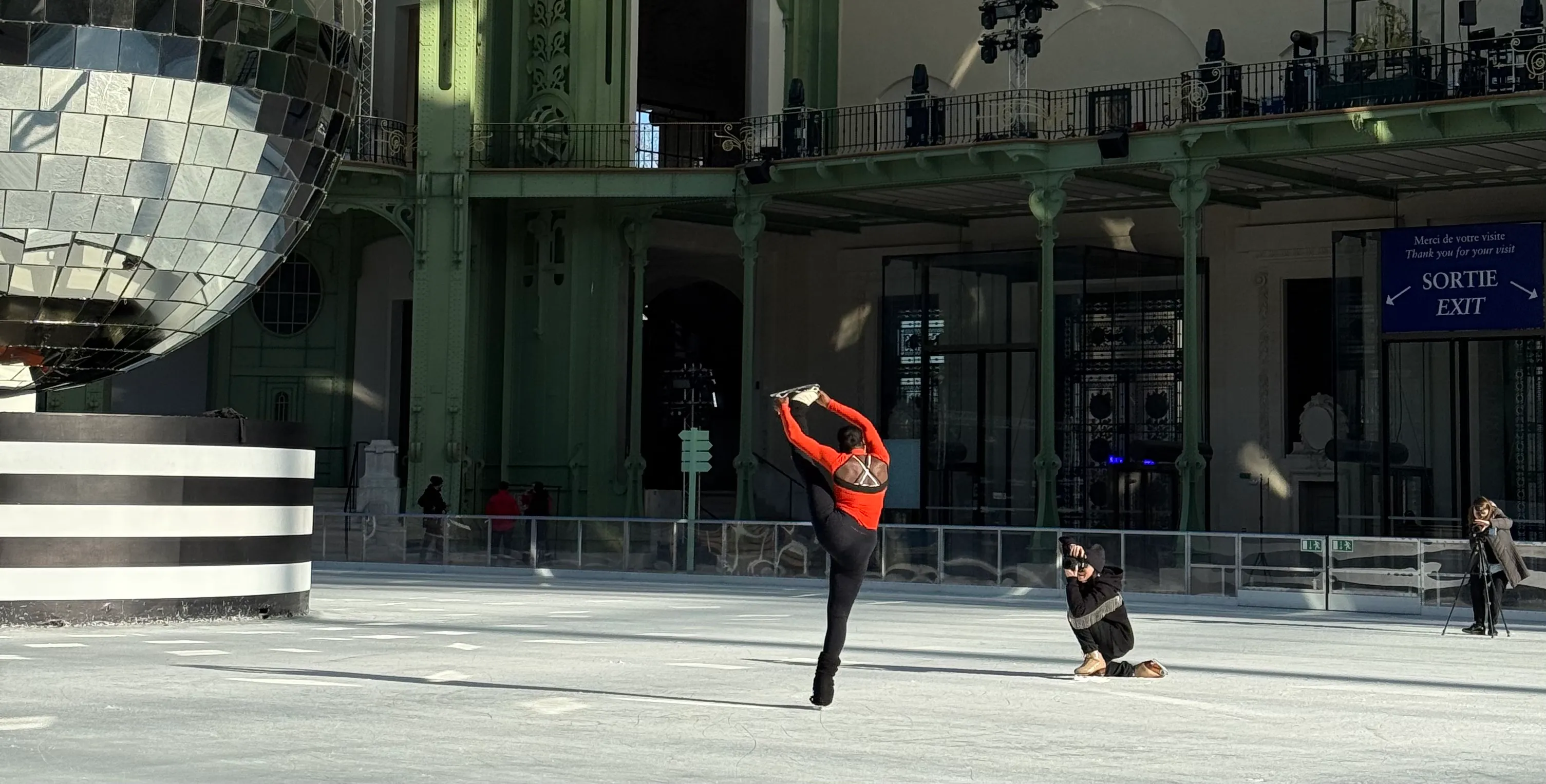 a figure skater in the centre. a photographer is taking photos of her. In the left you can see part of the disco ball