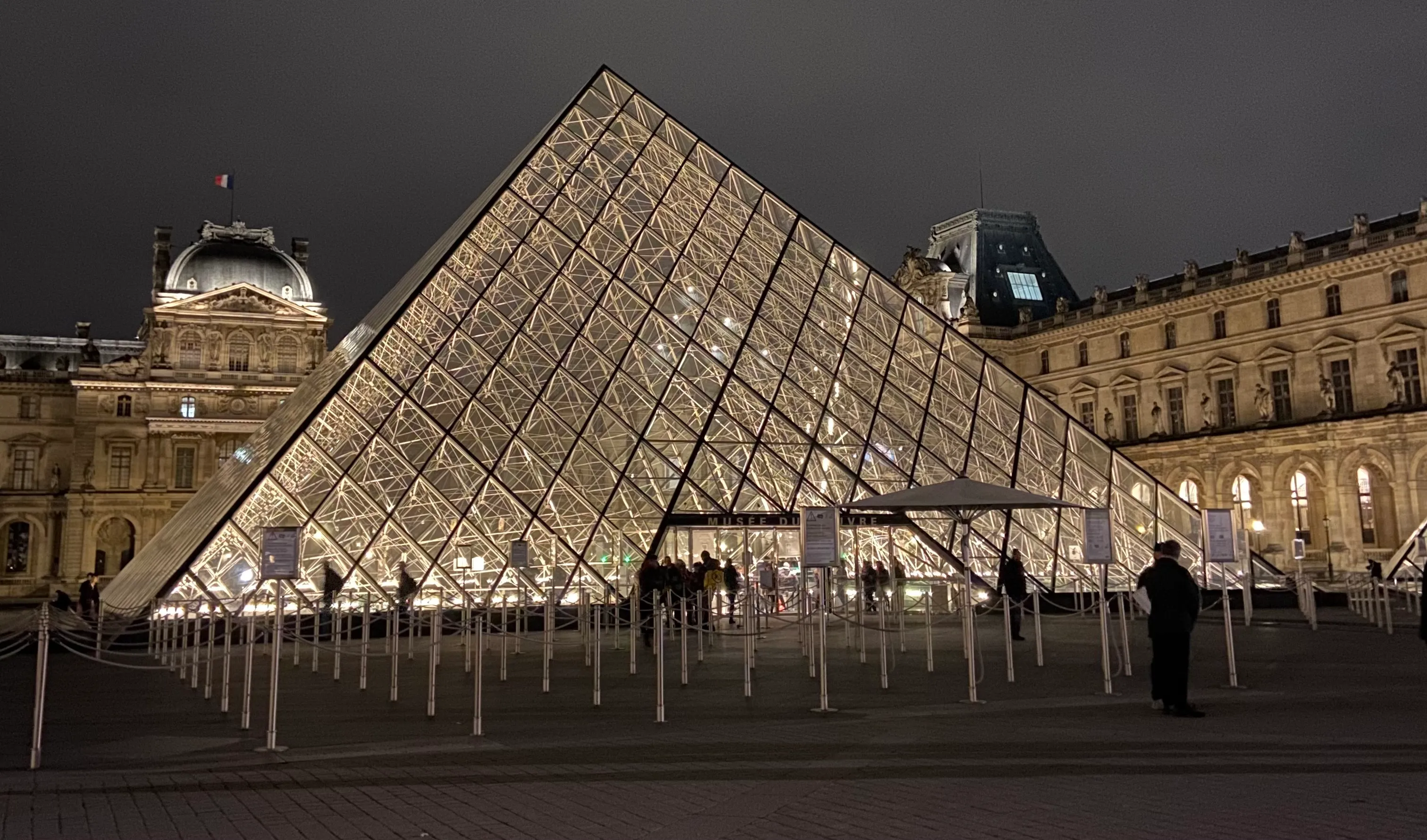 the outside of the Louvre in the evening. The sky is dark which makes the glass pyramid stand out