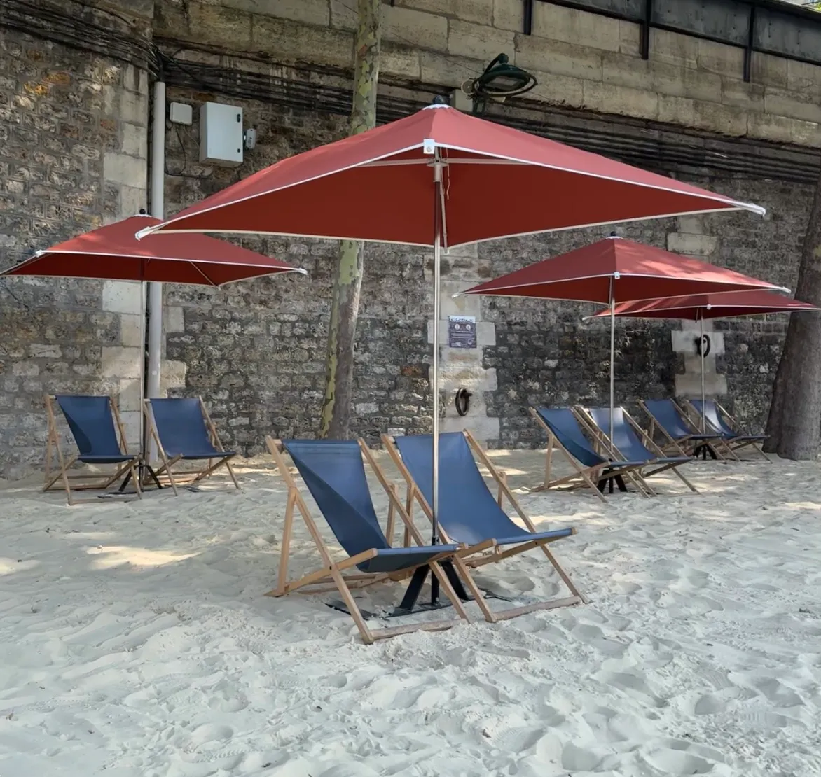 four sets of two blue deckchairs. The are on sand. Each set of deckchairs has a red parasol with them
