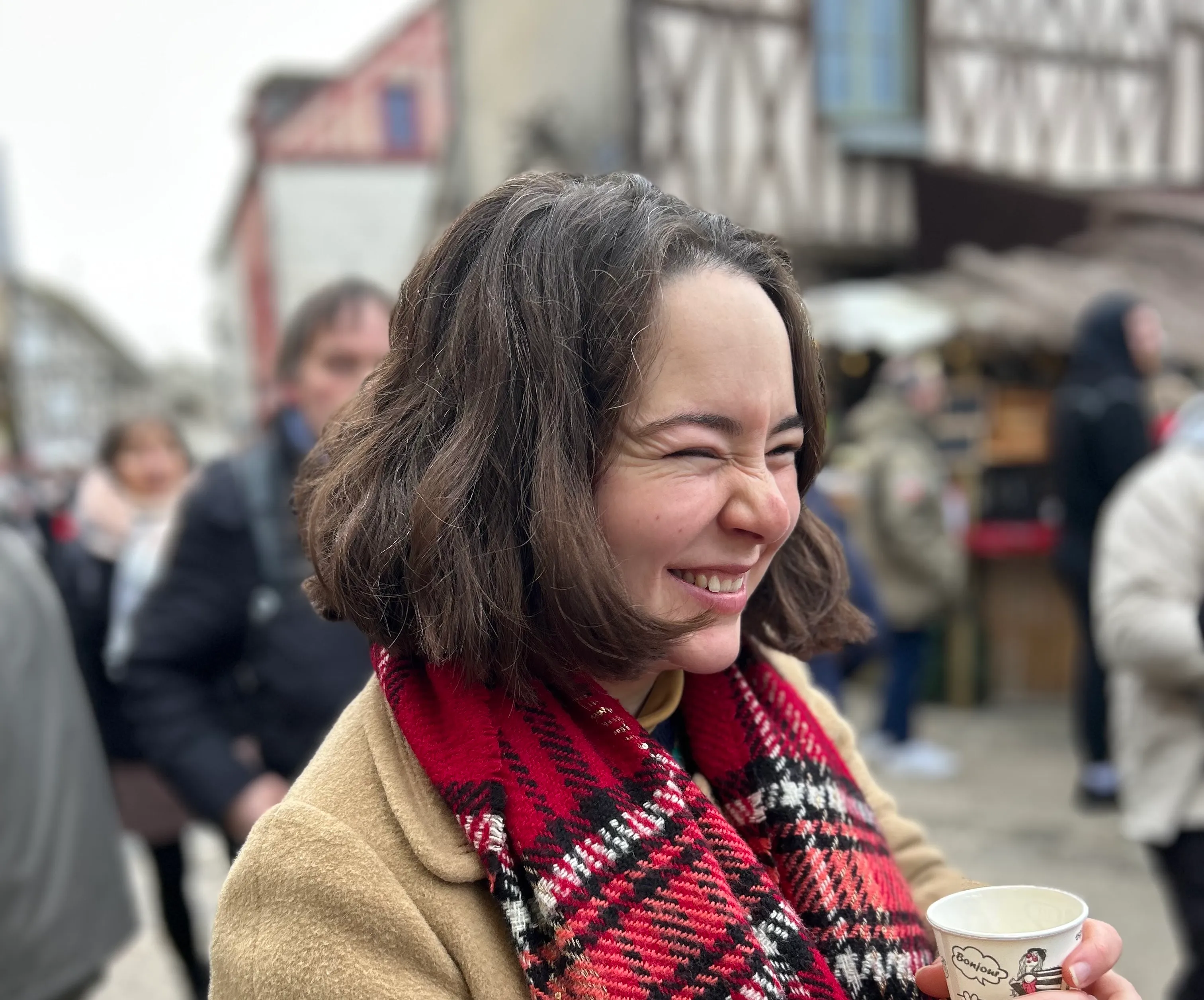 a woman with short brown hair, she is smiling. She is wearing a red scarf and holding a cup in her hand