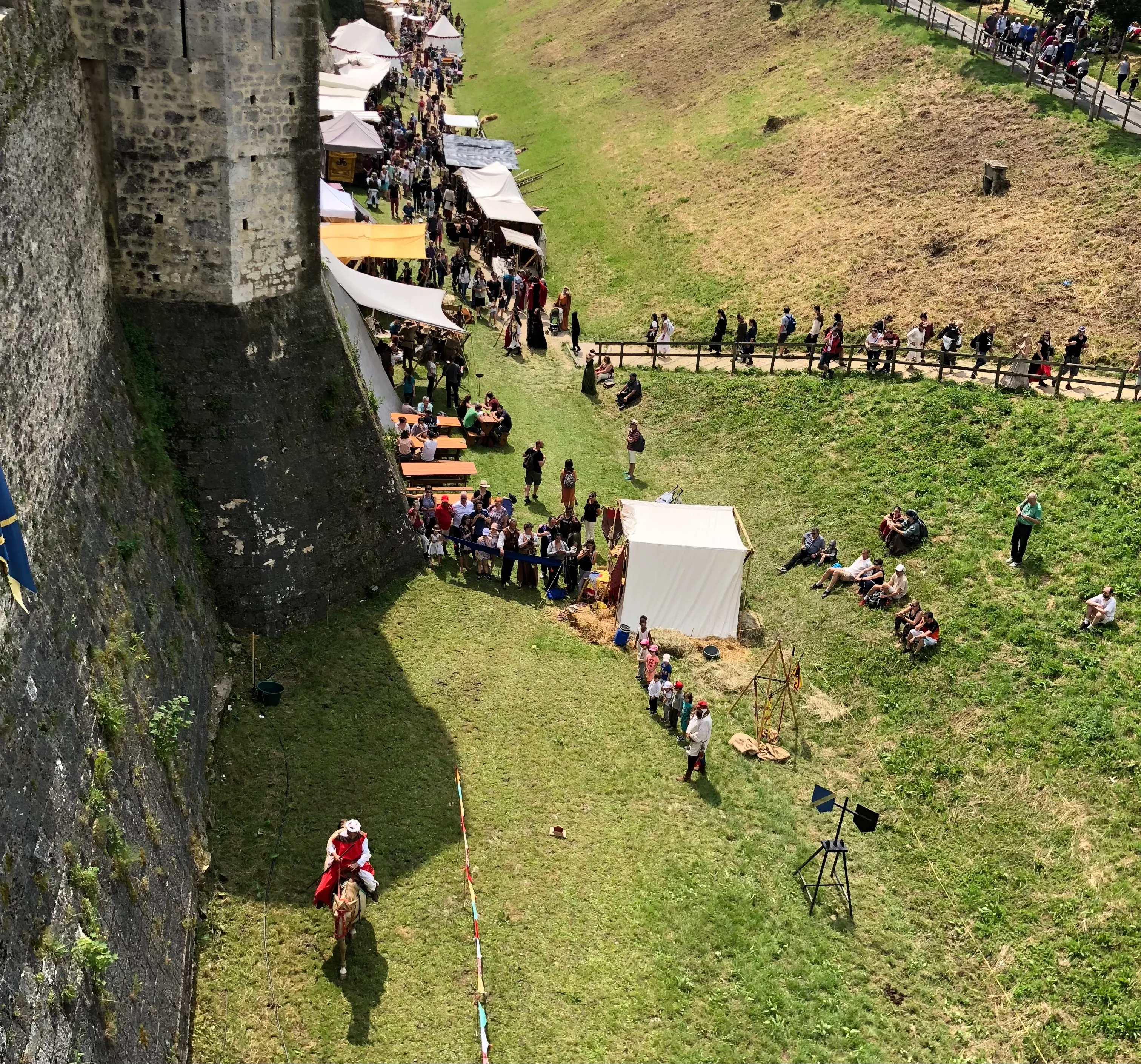 lots of people standing outside the city walls while visiting the medieval festival. There is someone riding a horse