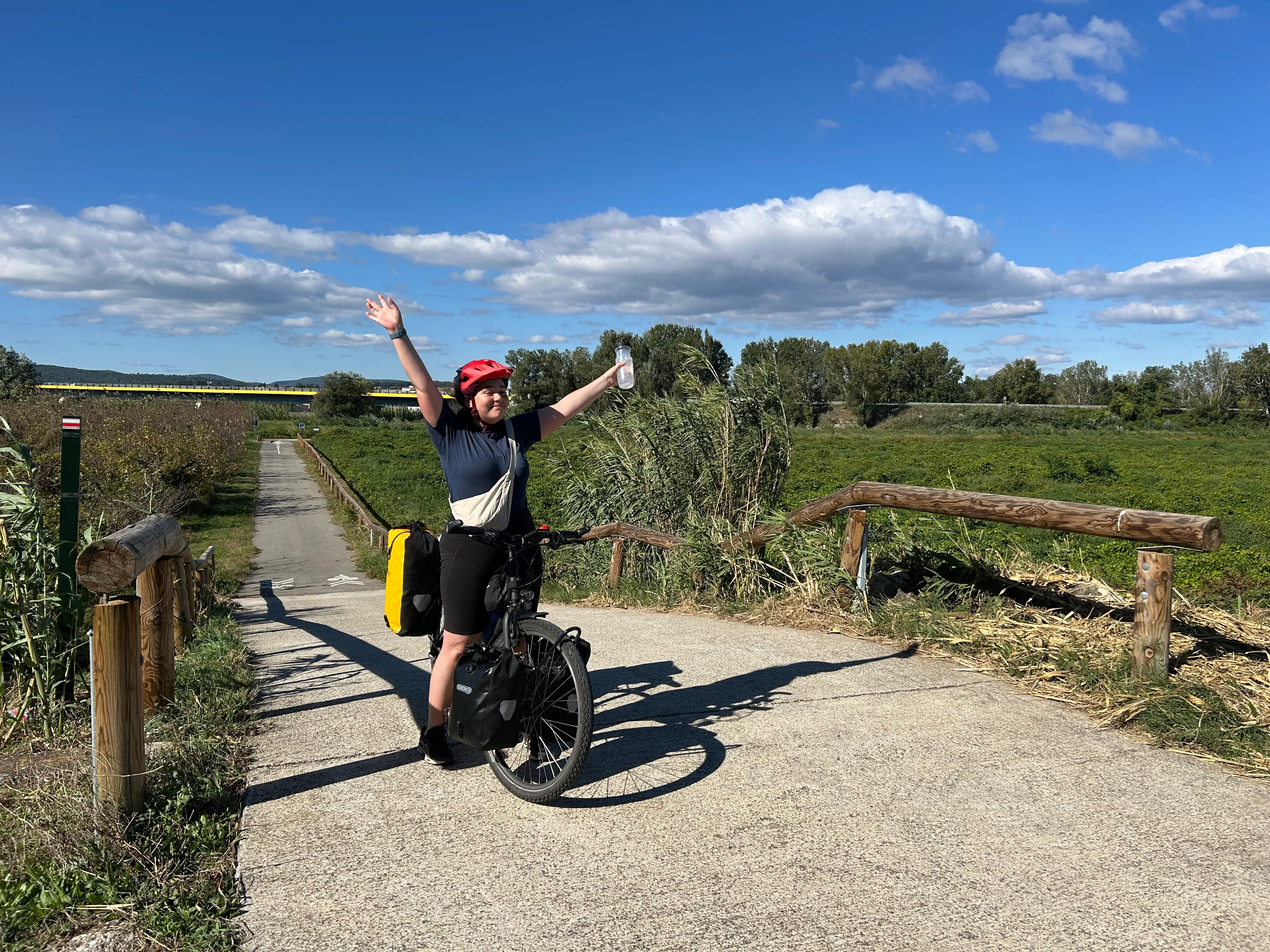 a woman with her hands up in the air, celebrating the journey so far. She is on a bike with four bike bags