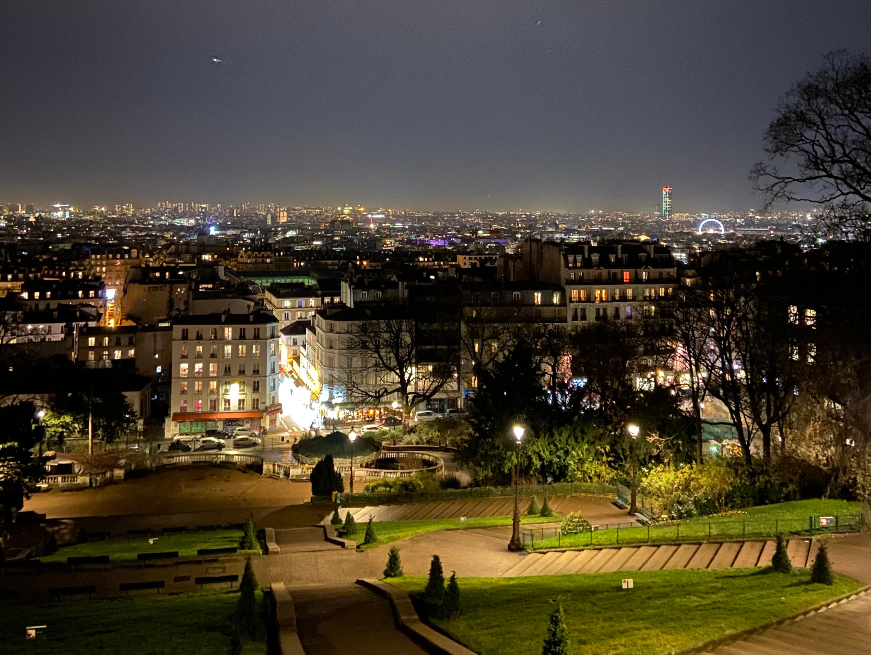 looking out across Paris from the bottom of the Sacre Cœur. The sun has set so the sky is dark. Most buildings have lights on